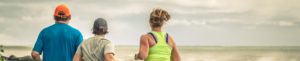 Three people running along the ocean. Two girls and one man jogging
